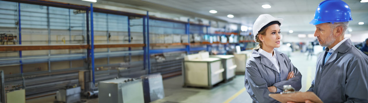 Mujer y hombre con cascos de seguridad conversan en un almacén industrial